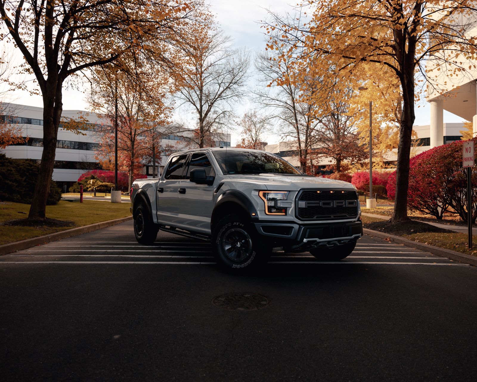 A modern pickup truck parked on a city street surrounded by autumn trees.